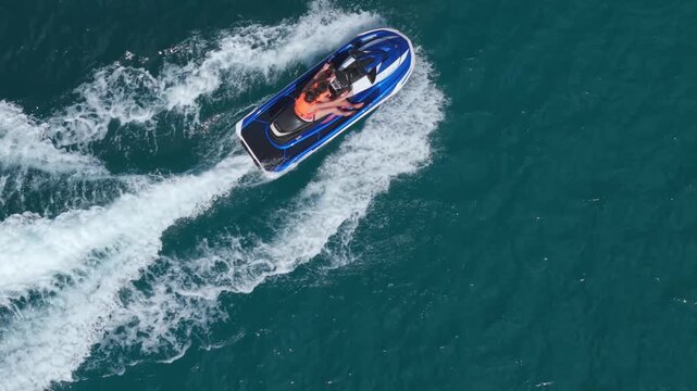 Direct top-down aerial view tracking a mother and daughter riding a blue jet ski, carving through deep turquoise waters at Beau Vallon, Seychelles with exploding white wakes.