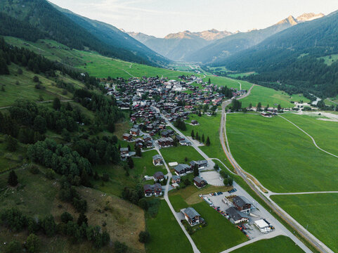 Goms, Switzerland - 09 August 2024: Aerial view of the village of Munster with traditional wooden houses surrounded by green meadows and high alpine peaks in the Goms valley.
