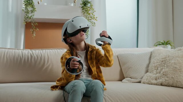 Concentrated little Caucasian child girl in vr glasses exploring metaverse internet technology at home living room enjoying game kid daughter in virtual reality headset playing in net service at home