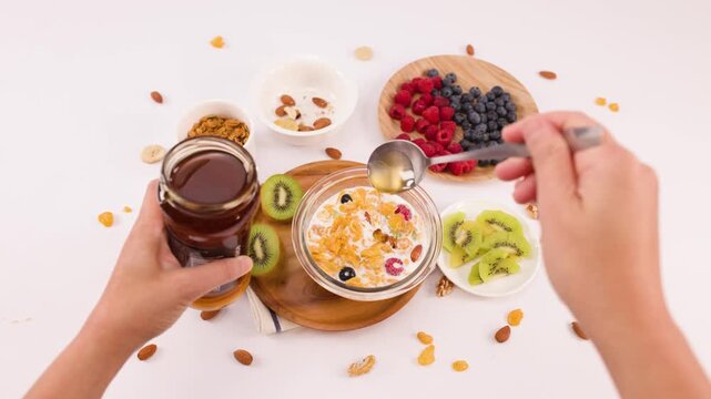 Drizzling Honey Over Cereal Bowl with Fresh Fruit and Berries