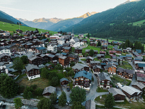 Goms, Switzerland - 09 August 2024: Aerial view of the village of Munster with traditional wooden chalets and a white church nestled in the green Goms valley of Valais.