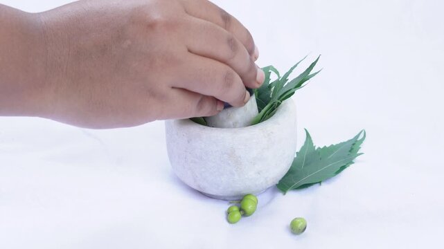 A woman hand holding a pestle and pounds neem leaves in a white stone mortar isolated on a white background. Herbal ayurvedic medicine making concept.