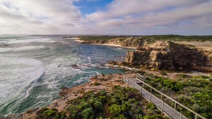 Obraz premium Aerial view of the Cape Northumberland coastline at Port Macdonnell, South Australia, revealing rugged shorelines, dark volcanic rock formations, and deep blue Southern Ocean waters shaped by wind and