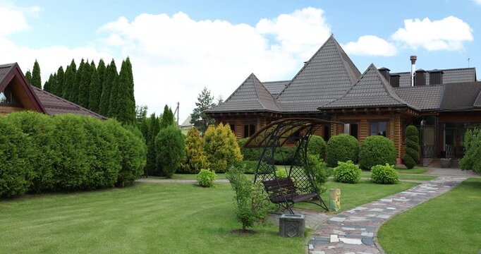 Luxury wooden cottage complex with beautiful landscaped garden and green lawn. Courtyard backyard of premium commercial real estate property with stone pathway and garden swing chair. Summer sunny day