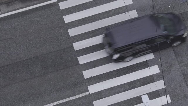 High angle view of a vehicle driving across a white pedestrian zebra crossing on the road.