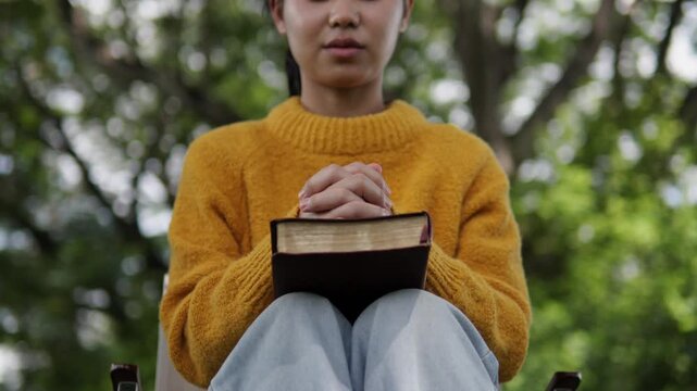 A young woman sits praying to God with her Bible, asking for a peaceful healing in her life healed by love and His holy word