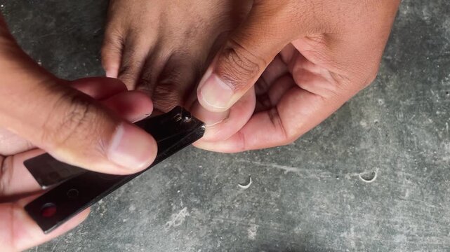 Close up of trimming toenails with nail clippers, personal hygiene routine showing foot care, grooming and self maintenance activity.