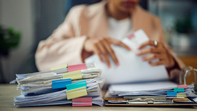 Woman reviews papers at cluttered desk. Fingers trace document edges. Stacks of folders rise beside her. Colorful clips hold each file. Focused, she organizes daily tasks. Ideal for business, finance