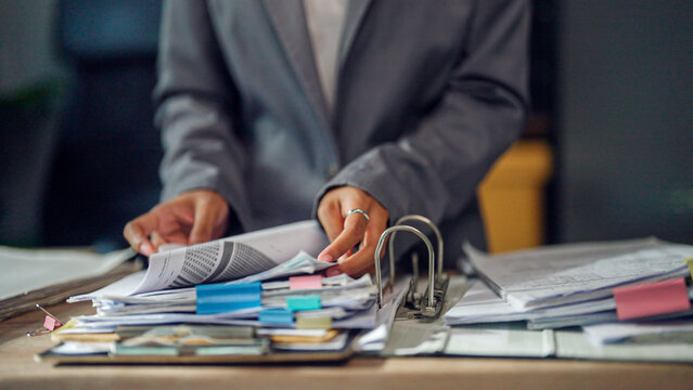 Professional hands sort through stacks of documents. Fingers grasp papers, ready to organize or analyze. Desk holds folders, pens, and clipped notes. Focused, calm, and deliberate-work in progress