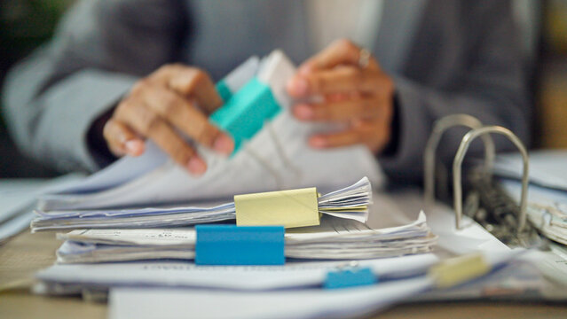 Hands organize papers with colorful clips and binders. Desk cluttered with documents suggests busy work or planning. Focused hands imply dedication to tasks or deadlines. Image conveys productivity