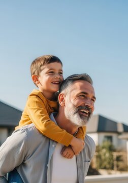 Happy Grandfather Giving Piggyback Ride to Grandson Outdoors in Residential Neighborhood