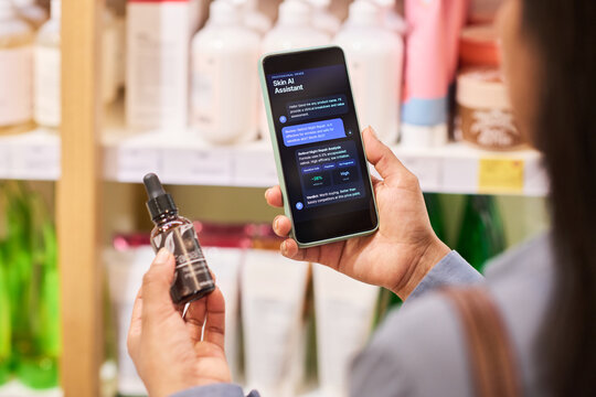 Over the shoulder shot of woman holding cosmetic serum and smartphone, comparing skincare product data in beauty store. Showing smart shopping, retail technology, consumer app marketing