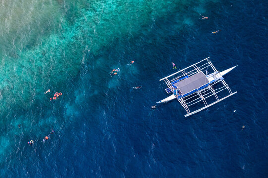 Moalboal, Philippines - 30 May 2026: Aerial view of a traditional outrigger boat and snorkelers near the coral reef drop-off in Basdiot.