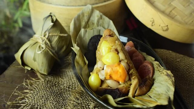 Steaming Zongzi or traditional Chinese rice dumpling with hot smoke. Delicious sticky rice wrapped in bamboo leaves filling with salted egg yolk, sausage, and mushrooms on plate.