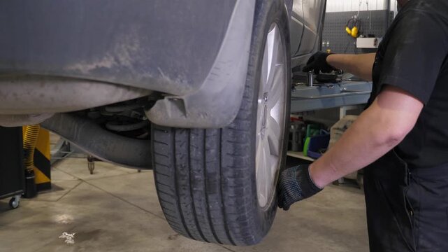 A mechanic repairs the wheels of a car at a service station. He removes or puts on fenders to the car, which is on a lift in the garage.