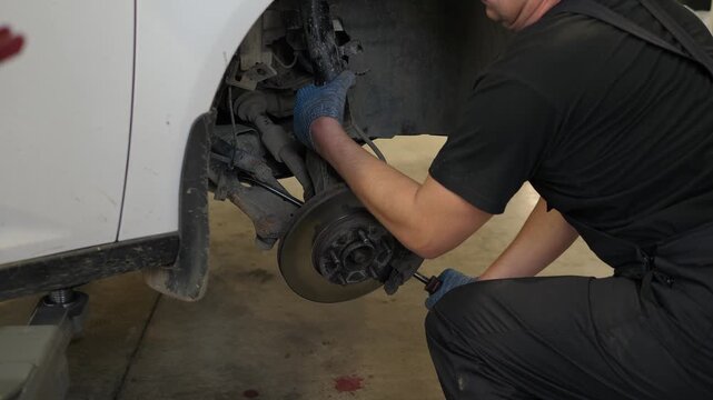 A close-up of a mechanic removes shock absorbers from a car that is lifted on a lift in an auto repair shop. Repair of shock absorbers in a modern service station.