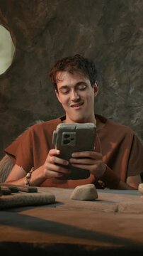 Funny Caveman Using Stone Smartphone and Expressing Joy in Prehistoric Cave