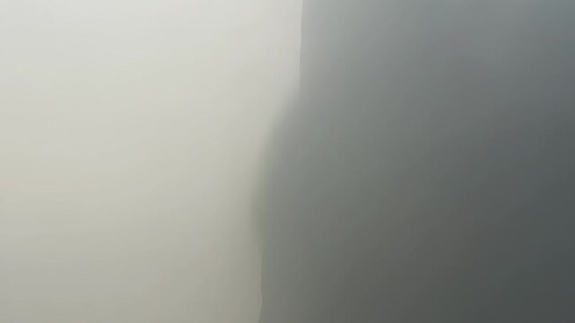 Thick fog moving over a dark mountain cliff in a moody landscape