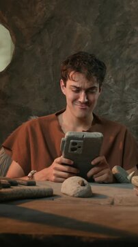 Funny Caveman Checking Stone Smartwatch and Working on Laptop in Prehistoric Cave