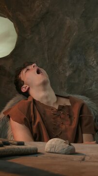 Funny Caveman Yawning and Feeling Tired in Front of Stone Laptop in Prehistoric Cave