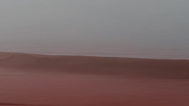 Red ocean waves rolling onto a misty shore under a hazy sky