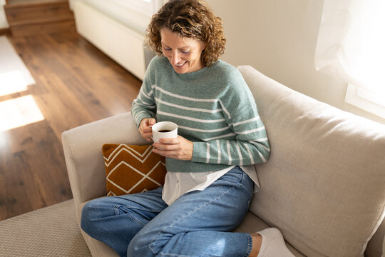 Woman relaxing on sofa drinking hot coffee at home