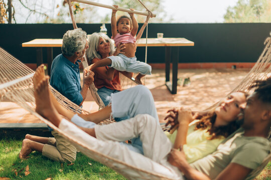 Multi-generational diverse family relaxing playing together in garden hammock