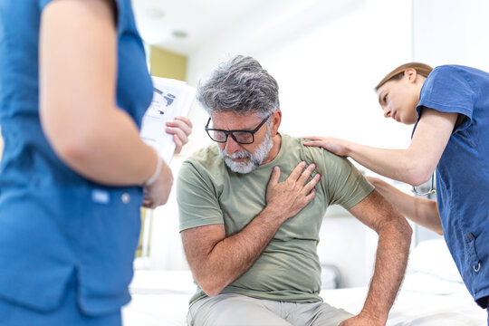 A concerned nurse and doctor provide care to an older male patient experiencing chest pain on a hospital bed. The team monitors the patient while reviewing medical documentation 