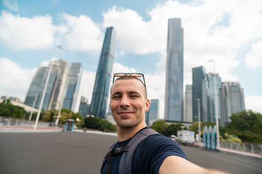 Young man taking selfie in guangzhou, china, facing ifc tower and other modern skyline skyscrapers, urban travel concept