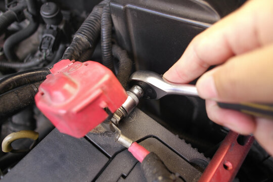 Hand using a ratchet wrench to loosen or tighten a bolt on a car battery terminal during automotive repair