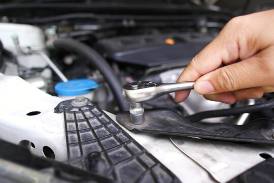 Hand using a socket ratchet wrench to tighten or loosen a bolt under a car hood during routine vehicle maintenance and engine repair