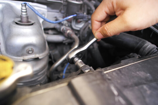 Hand using a socket ratchet wrench to loosen or tighten a bolt in a car engine bay during automotive maintenance and repair