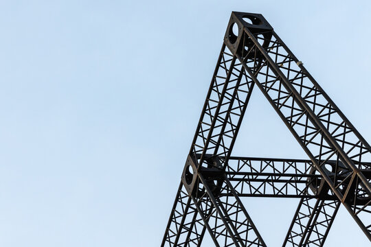 Black steel truss framework forming triangular lattice shapes against a clear blue sky, highlighting industrial construction geometry, texture and engineering detail in a minimal architecture