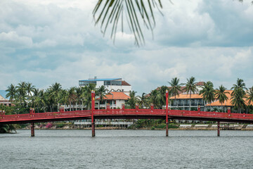 Obraz premium Red wooden pedestrian footbridge over a wide river in a tropical country