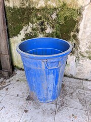 Fototapeta premium Large blue plastic bucket or trash bin placed outdoors against a mossy concrete wall.