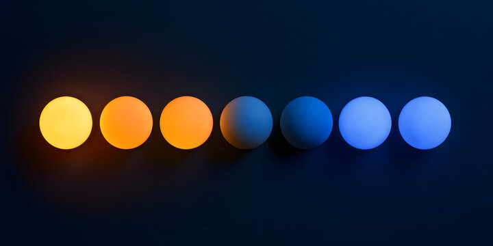 A line of circular lights or lamps with varying kelvin color temperatures ranging from a warm orange to a cool blue set against a dark backdrop, photographed in a flat lay with the top viewed from abo