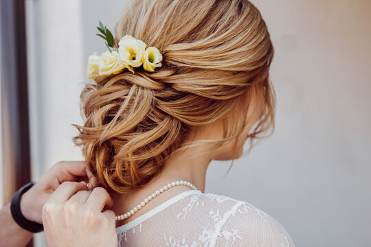 Bridal updo hairstyle adorned with cream flowers and pearls. Elegant wedding hair styling, sophisticated bride look, romantic morning preparation, formal occasion hairdo 