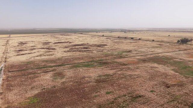 Aerial drone footage flying over the arid and dry landscape surrounding Lemoore College in California. Showcasing vast fields and plains under a hazy sky. Highlighting the state's drought conditions