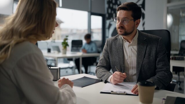 Caucasian leader of company businessman leading business interview writing notes talking with businesswoman candidate woman boss male review resume hiring job female intern two people talk in office