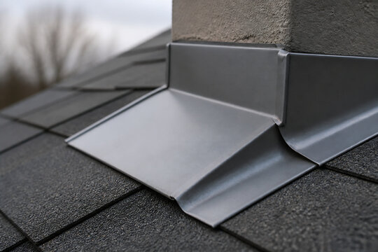 A metal flashing piece is installed on a dark shingled roof near a building edge.