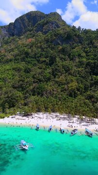 Drone aerial view of Seven Commandos Beach in El Nido, Palawan, Philippines. Tropical shoreline with turquoise water, white sand and limestone cliffs.