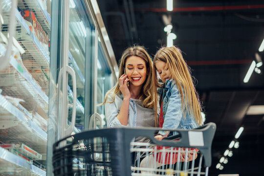 Mother talking on phone, shopping with daughter at supermarket