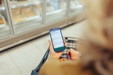 Woman holding smartphone with shopping list app in supermarket
