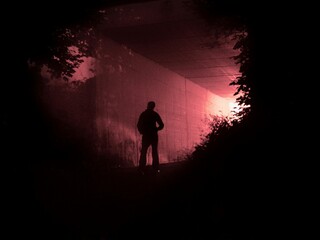 Fototapeta premium Dramatic silhouette of lonely man in dark tunnel under red light evoking mystery, danger, and suspense for cinematic thriller posters.