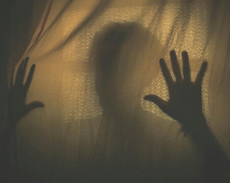 Mysterious blurry silhouette of hands pressing against textured fabric curtain evoking fear panic and deep psychological isolation