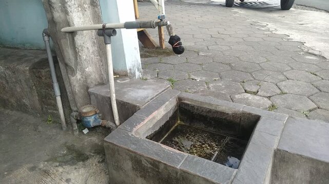 Water dripping from an outdoor public tap with a traditional cloth filter into a concrete basin.