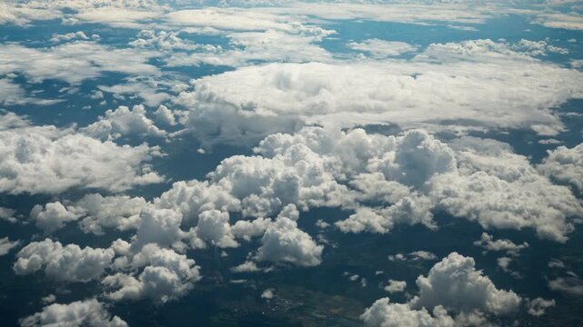 Dense white cumulus clouds float over land fields in high altitude aerial view from a commercial passenger airplane window during transit flight travel for global transport ecology concept.