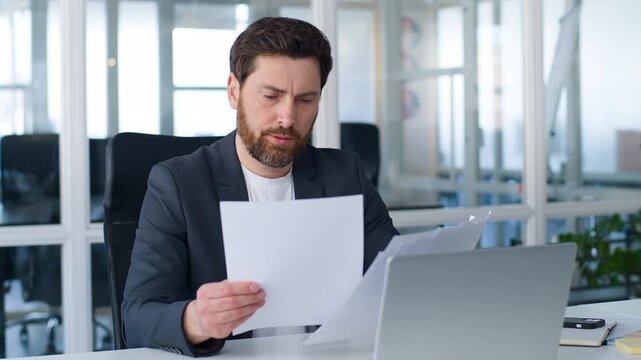 Serious Caucasian middle-aged business man reading letters bank correspondence negative shaking head papers mistake male boss mature businessman with documents checking reports dissatisfied in office