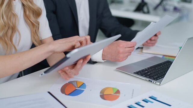 Cropped view Caucasian business colleagues working with documents laptop and digital tablet at office meeting in boardroom unrecognizable businessman holding papers businesswoman using device teamwork