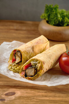 Vegetarian tofu wrap or shawarma cut in half on parchment paper, rustic wooden background. Vertical high angle view.